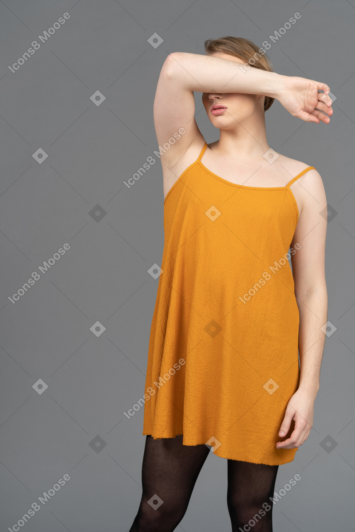 Young queer person in orange dress covering face
