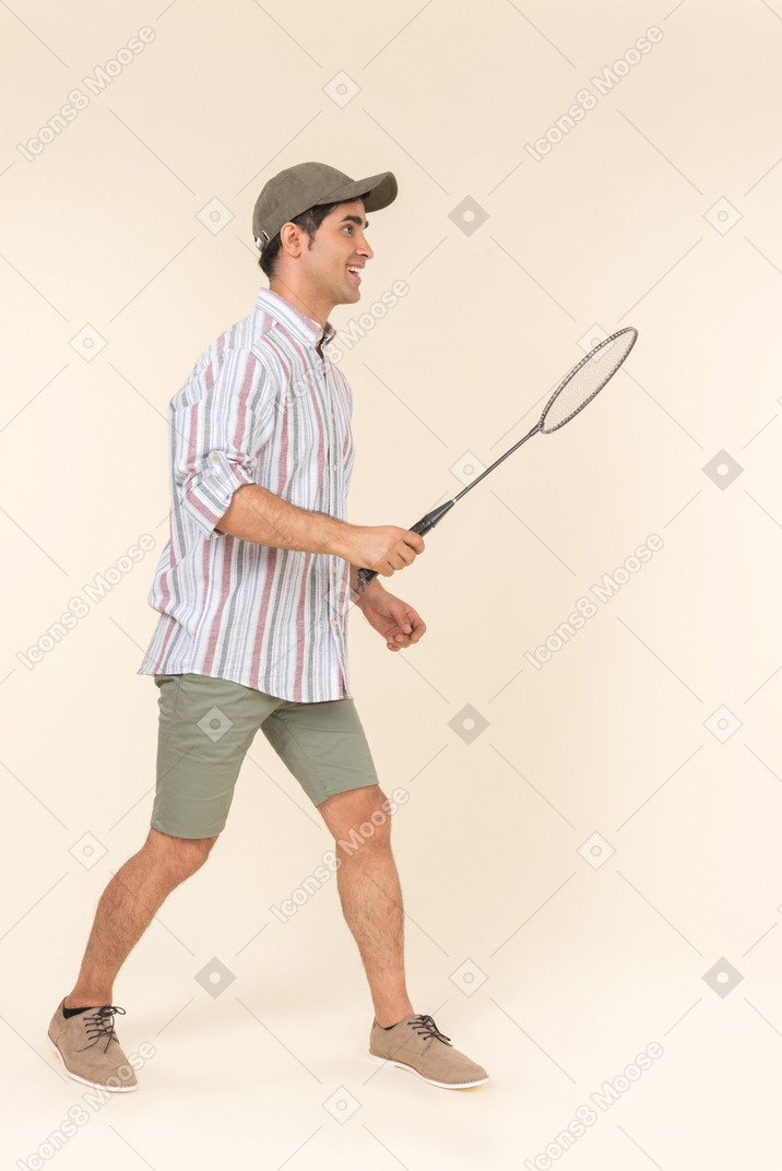 Jovem caucasiano em pé de perfil e segurando a raquete de tênis