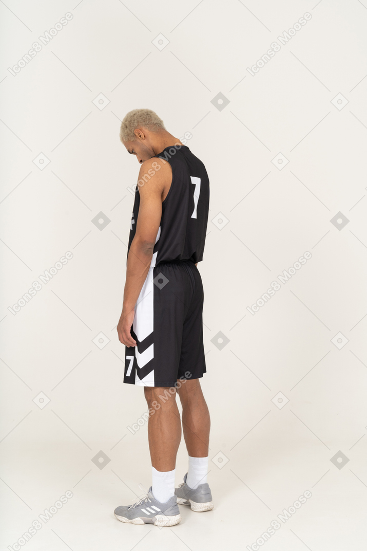 Vista posterior de tres cuartos de un joven jugador de baloncesto masculino cansado mirando hacia abajo