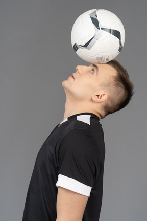 Vista lateral de um jogador de futebol masculino segurando uma bola na cabeça