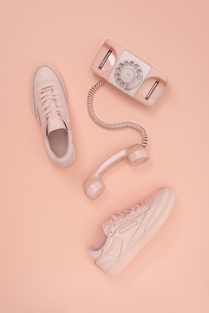 Pink sneakers and pink telephone on pink background