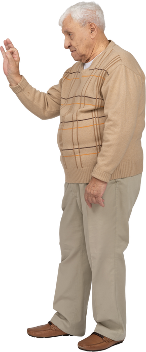 Vista lateral de un anciano con ropa informal que muestra el signo de ok