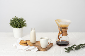 Chemex, große tasse kaffee, kekse und eine flasche milch auf dem tablett und pflanze im topf