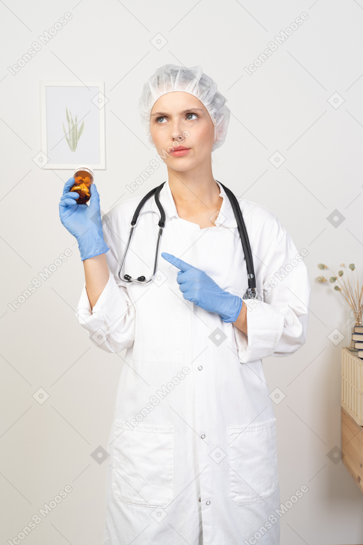 一位困惑的年轻女医生拿着一罐药丸的前视图