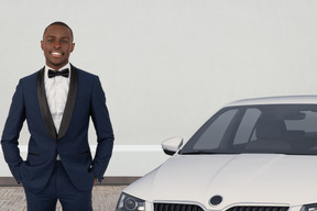 A man in a tuxedo standing next to a white car