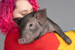 Pinkhaarige frau, die ein kleines ferkel hält