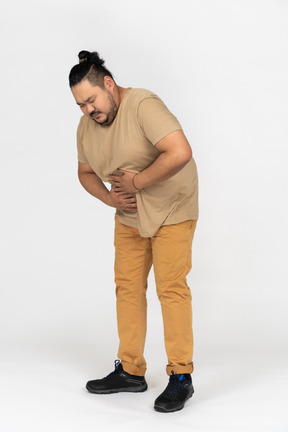 Homem asiático gordo, sofrendo de dor de estômago e segurando sua barriga com as duas mãos