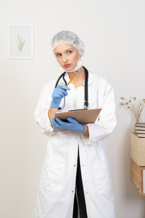 Vista frontal de uma jovem médica segurando um tablet e apontando para o lado
