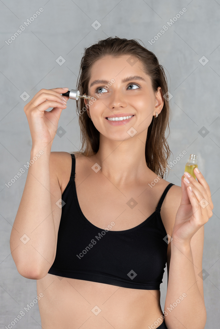 Portrait d'une jeune femme qui a l'air heureuse en utilisant de l'huile pour le visage