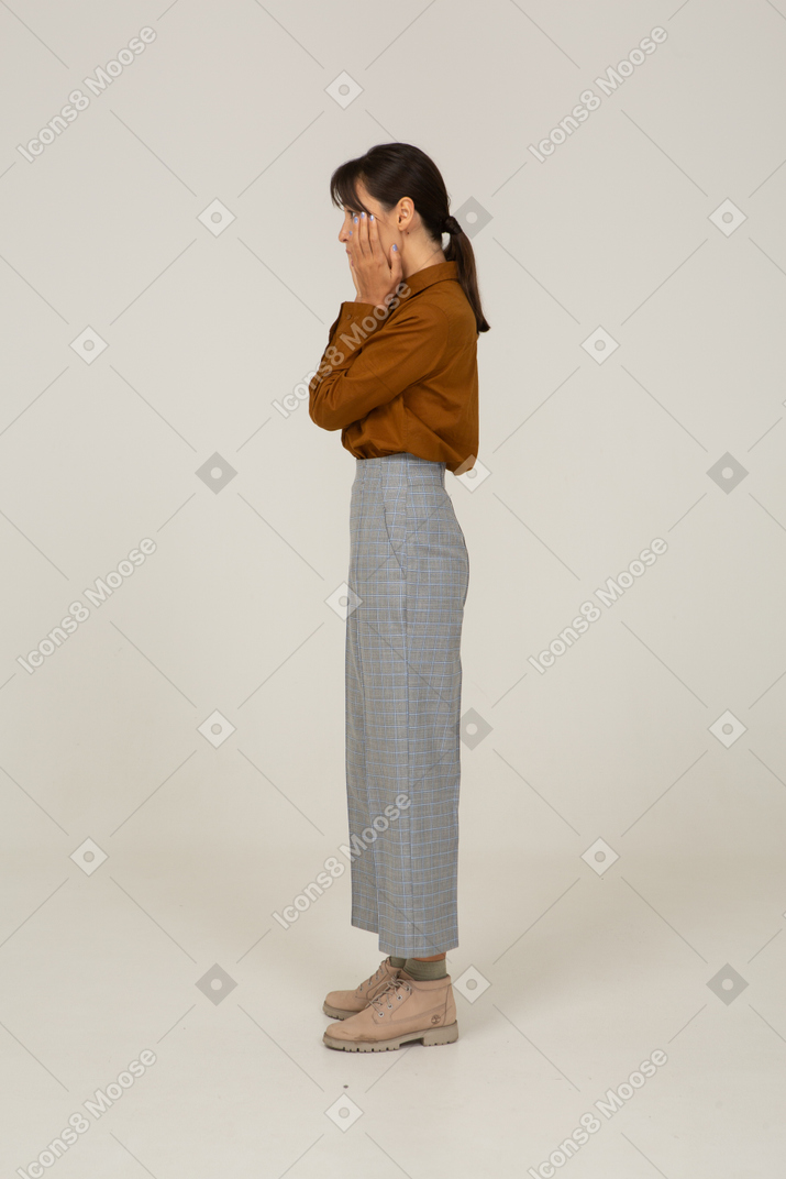 一位身着马裤和衬衫的年轻亚洲女性抚摸她的脸的侧视图