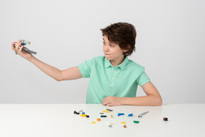 Ragazzo teenager in maglietta polo verde che gioca con il set di costruzione