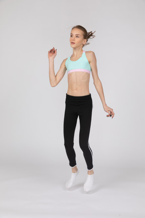 Вид в три четверти девушки-подростка в спортивной одежде, поднимающей руку во время прыжка