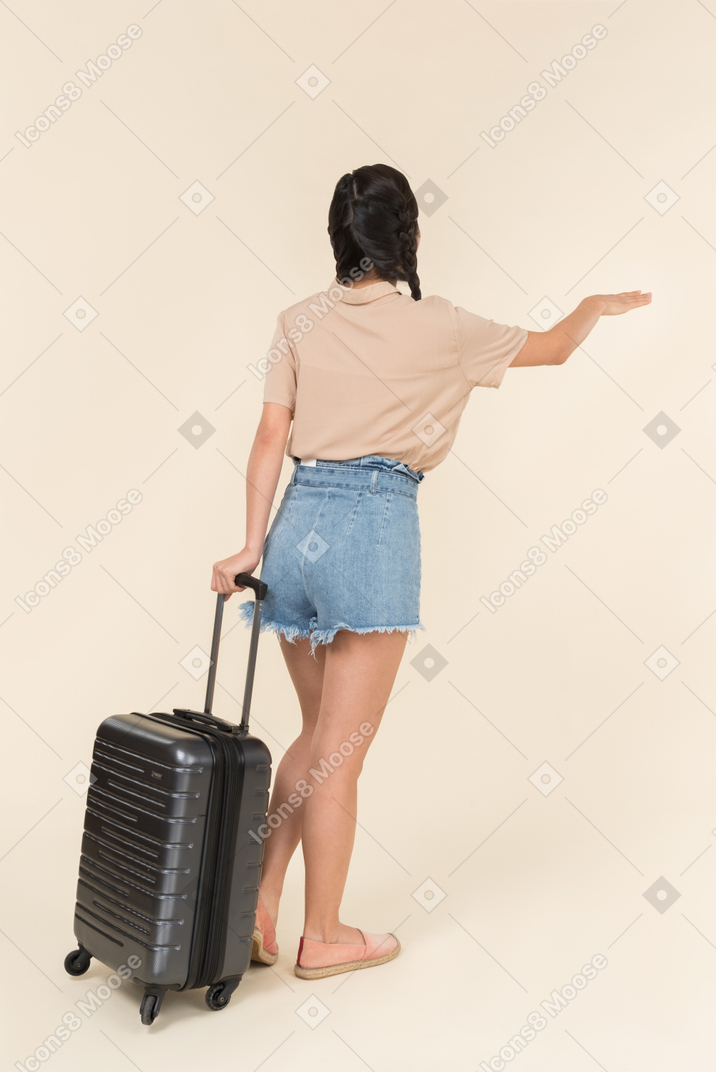 タクシーを呼ぶスーツケースを持つ若い女性