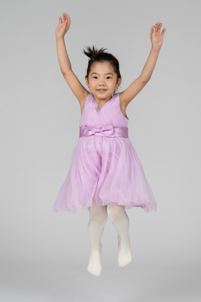 Garota feliz em um vestido rosa pulando e olhando para a câmera