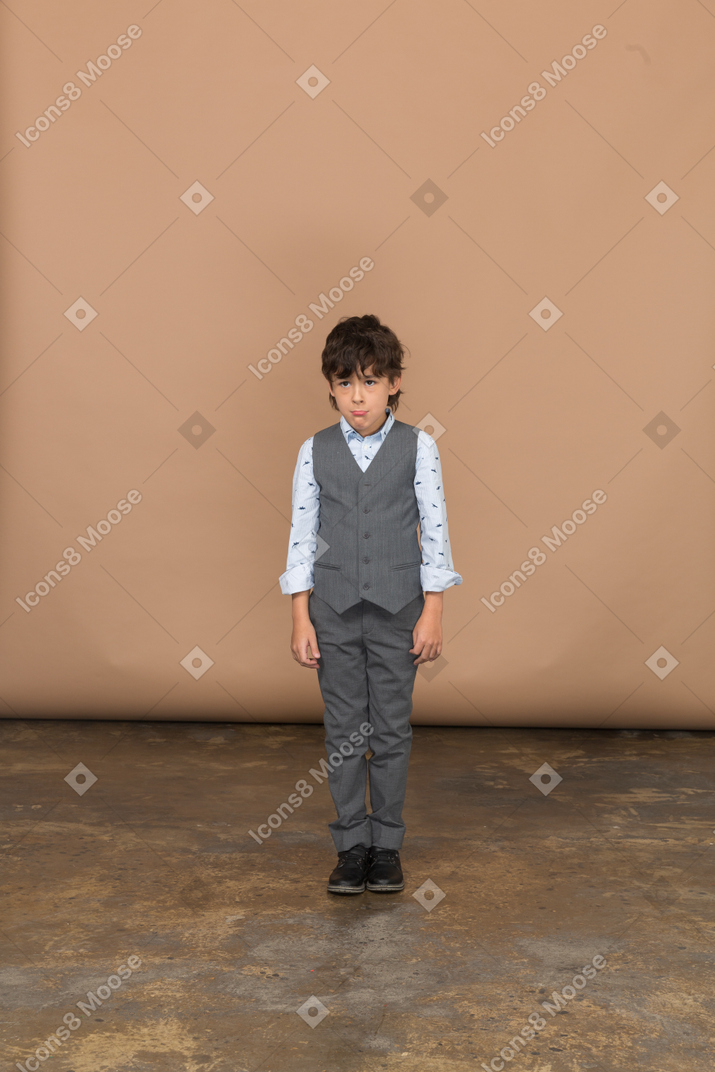 Vista frontal de un niño en traje mirando a la cámara y haciendo muecas