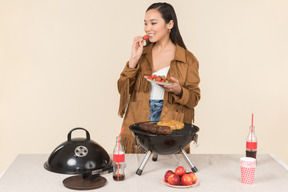 Young asian woman standing near grill and throwing a fruit