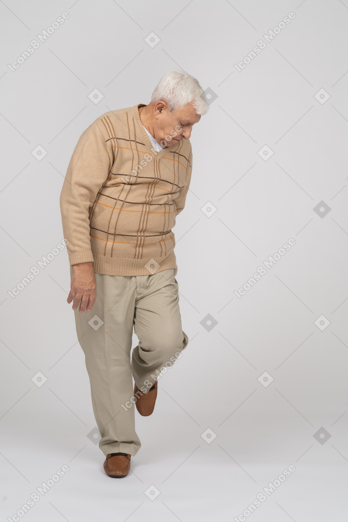 一位穿着休闲服的老人站在一条腿上向下看的正面图