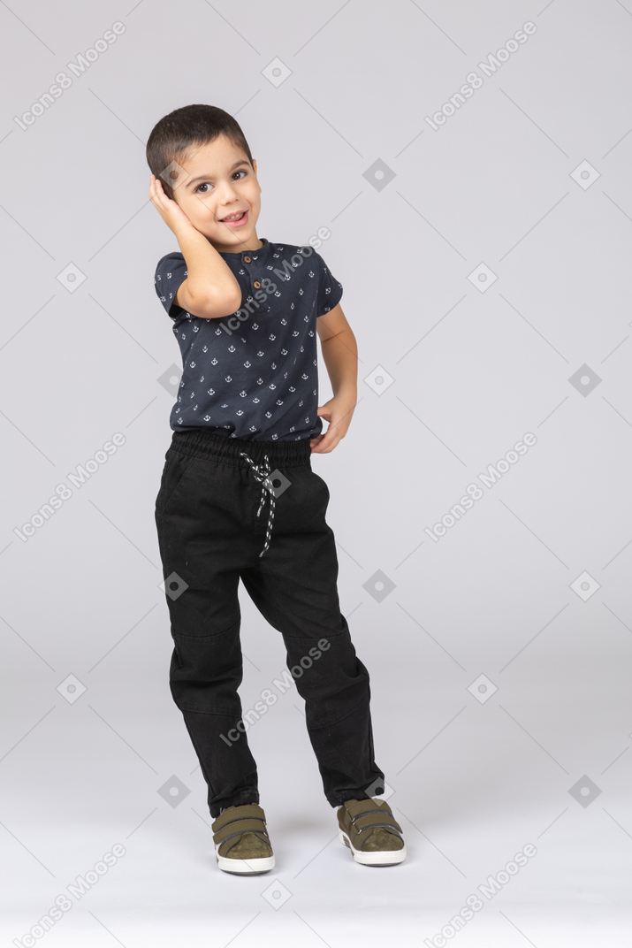 Vista frontal de um menino feliz cobrindo a orelha com a mão e olhando para a câmera