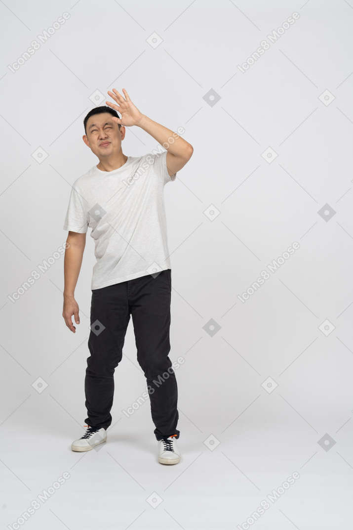 Vista frontal de um homem em roupas casuais em pé com a mão levantada e olhando para cima