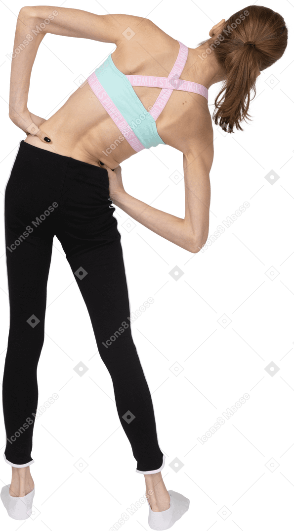 Vista posterior de una jovencita en ropa deportiva poniendo las manos en las caderas mientras se inclina hacia la derecha
