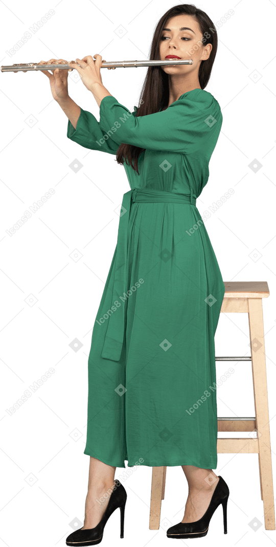 Pleine longueur d'une jeune femme en robe verte assise sur une chaise tout en jouant de la clarinette