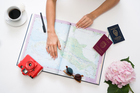 Manos femeninas junto al mapa, cámara roja, taza de café, pasaportes y gafas de sol.