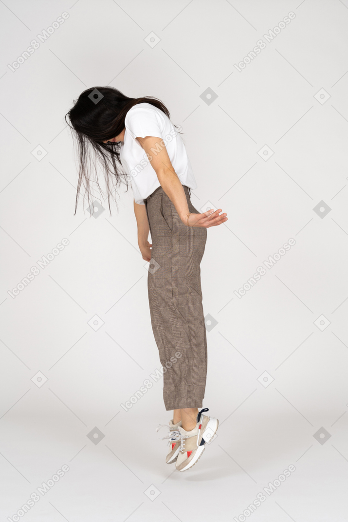 Vista laterale di una giovane donna che salta in calzoni e t-shirt guardando verso il basso
