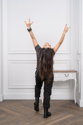 Vista posterior de una mujer joven inclinándose hacia atrás y mostrando gesto de rock