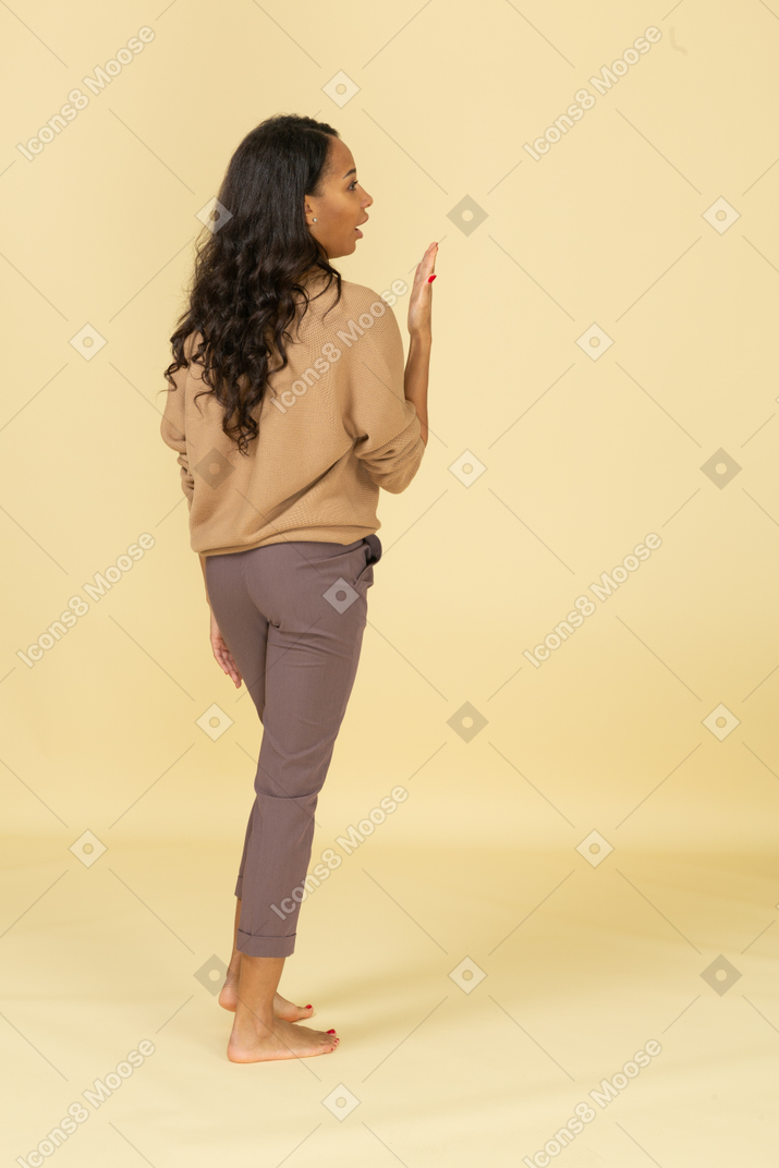 Back view of a talking young dark-skinned female raising her hand