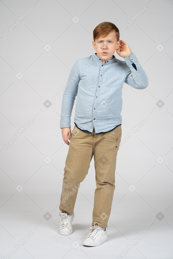 Front view of a boy keeping hand near ear and listening attentively