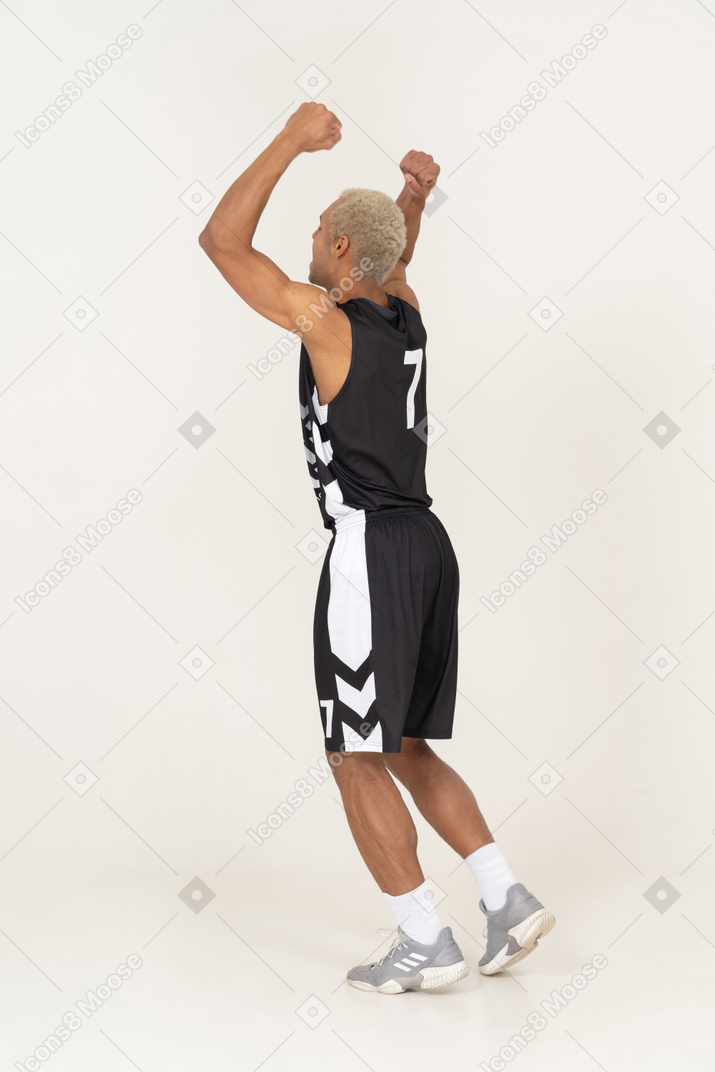 Three-quarter back view of a happy young male basketball player raising hands