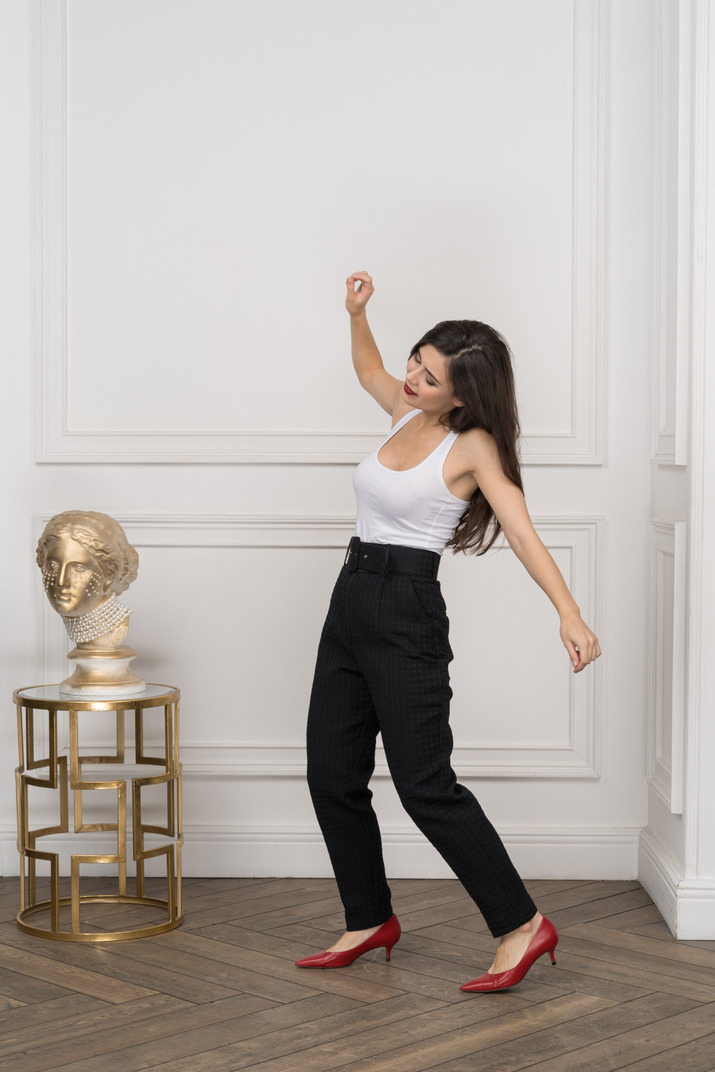 Full-length of a young female raising hand and stepping to a golden greek sculpture