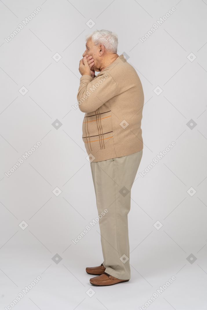 Side view of an old man in casual clothes covering mouth with hands