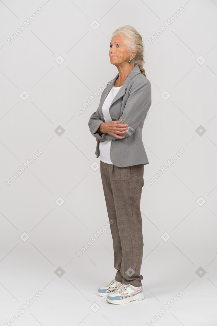 Вид сбоку пожилой женщины в сером пиджаке, позирующей со скрещенными руками