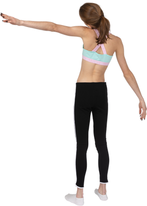 Vista posterior de tres cuartos de una jovencita en ropa deportiva extendiendo su mano e inclinando la cabeza