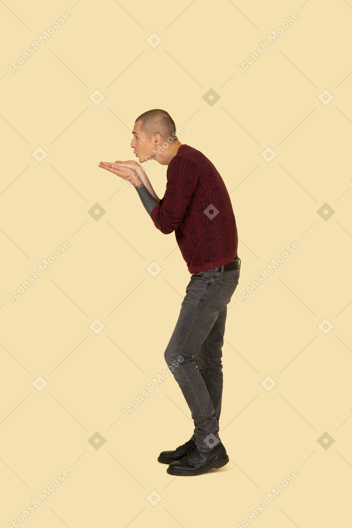Seitenansicht eines jungen mannes im roten pullover, der einen luftkuss sendet