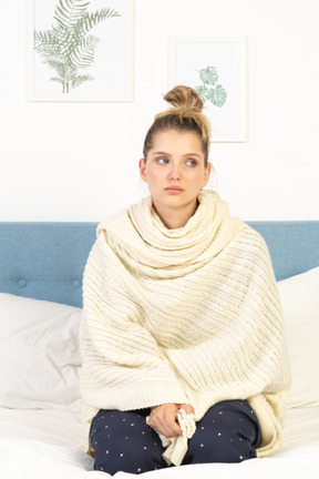 Vue de face d'une jeune femme enveloppée dans une couverture blanche assise dans son lit