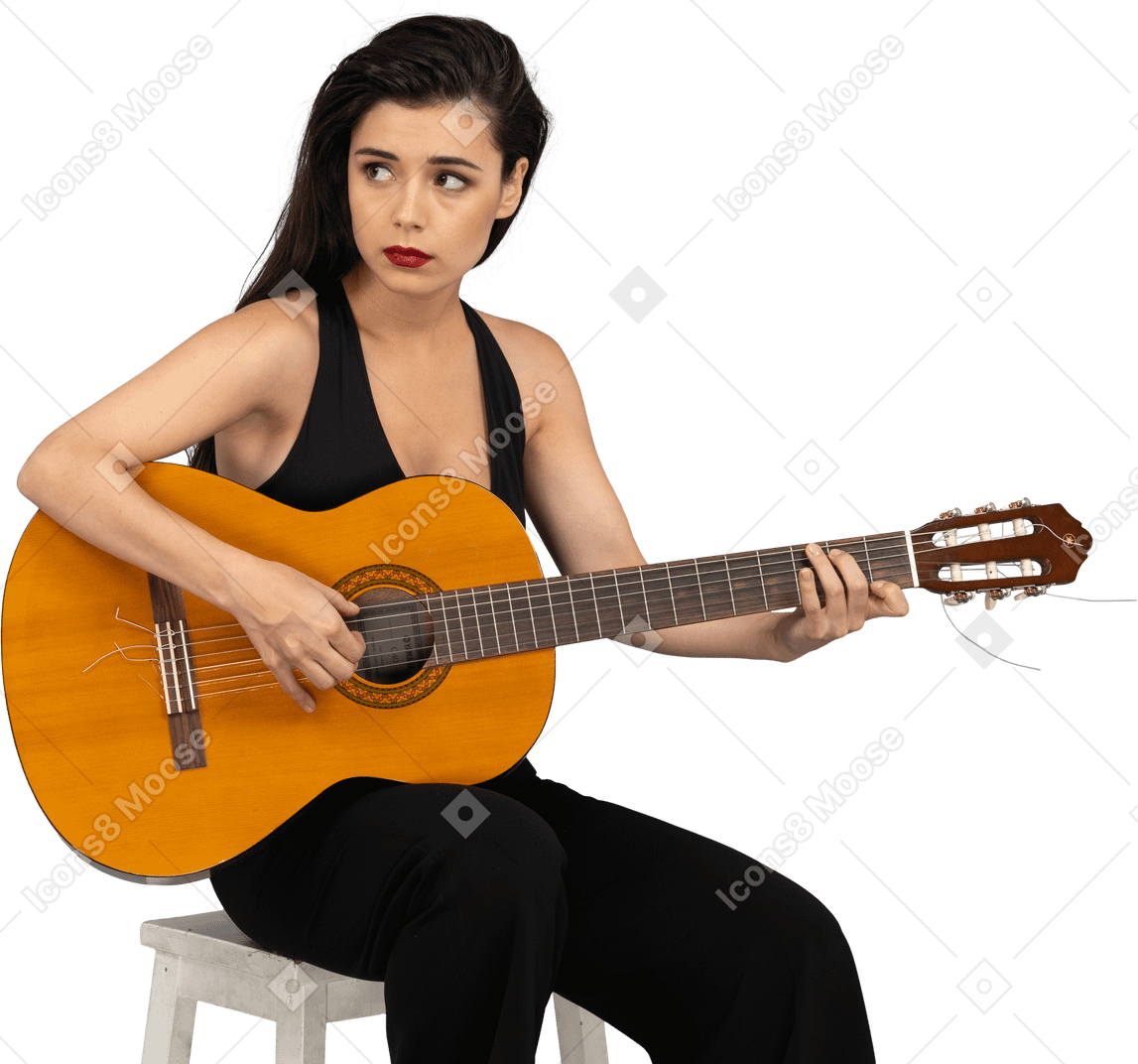 Front view of a sitting young lady in black suit playing guitar and looking aside