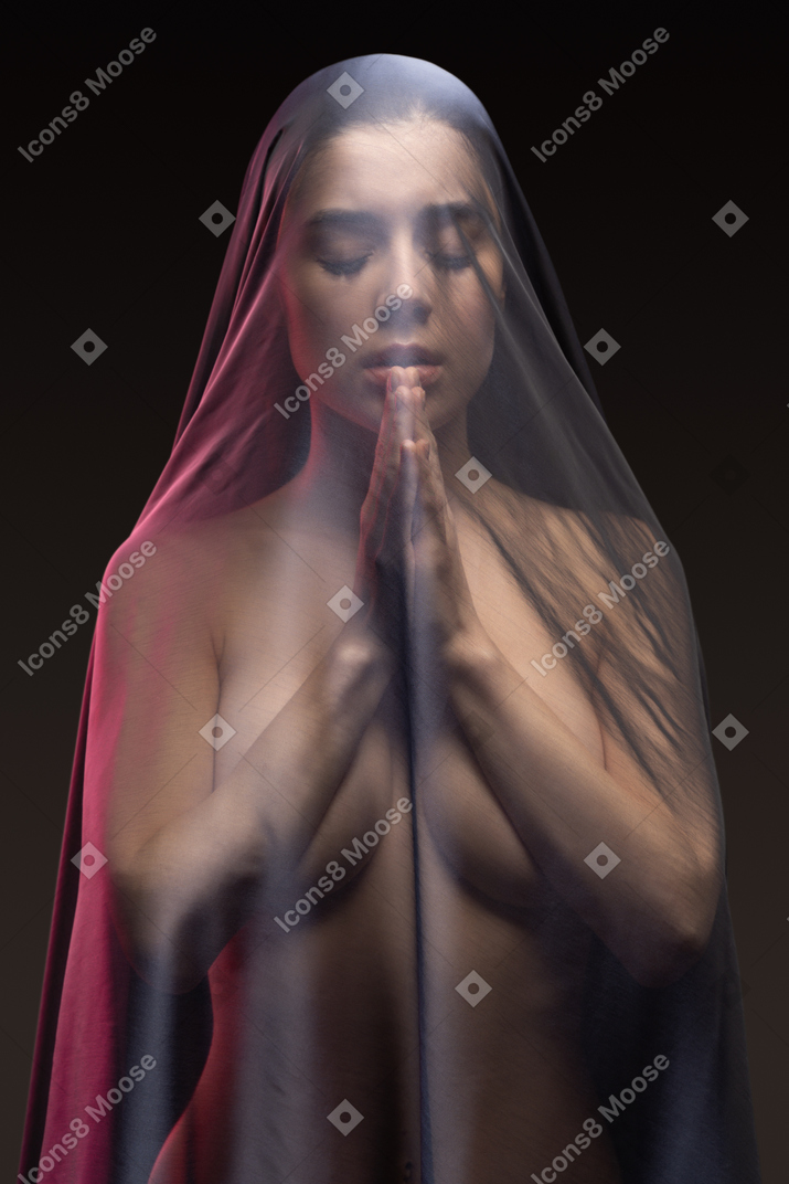 Sensual naked young woman praying in dark veil