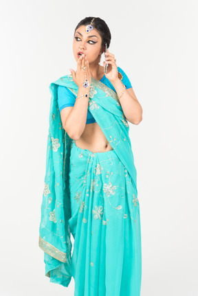 Young indian dancer in blue sari closing mouth and talking on the phone