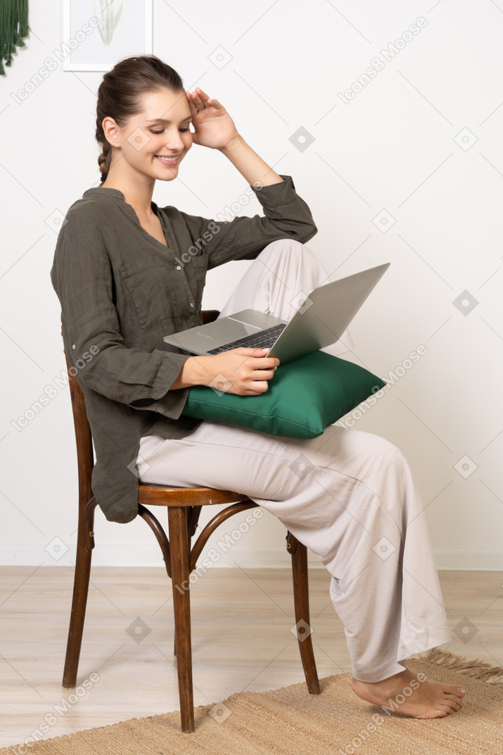 노트북과 함께 의자에 앉아 집 옷을 입고 젊은 여자의 측면보기