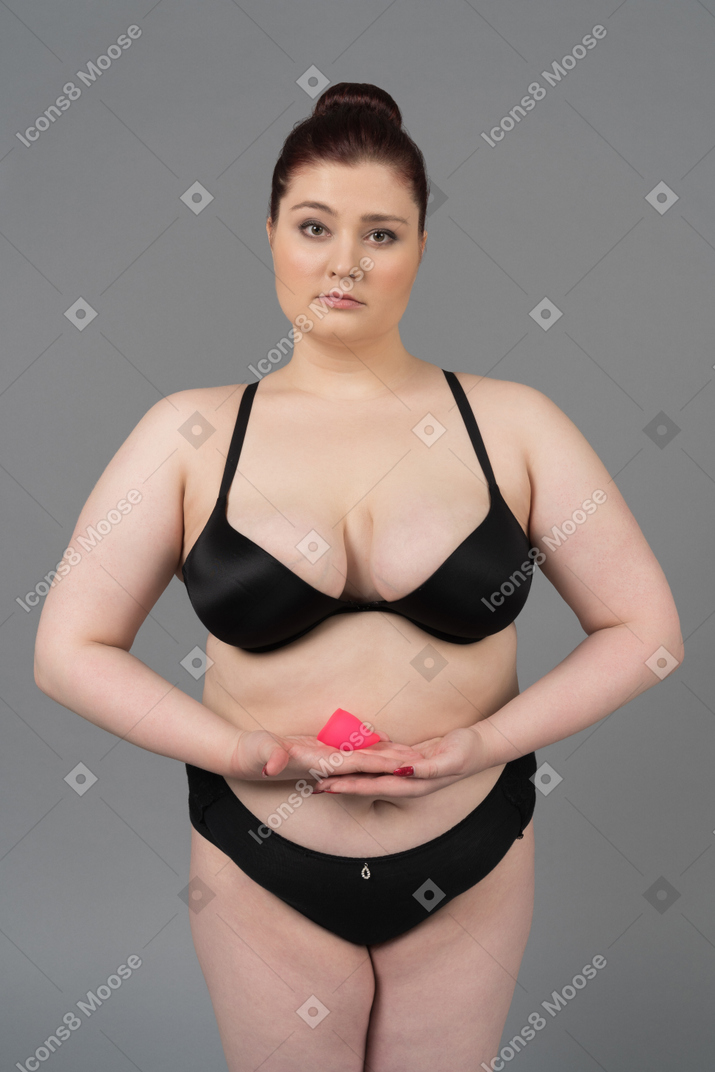 Body positive woman in black lingerie holding pink menstrual cup