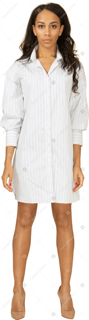 Vista frontal de una mujer joven de piel oscura confiada en vestido blanco mirando a la cámara