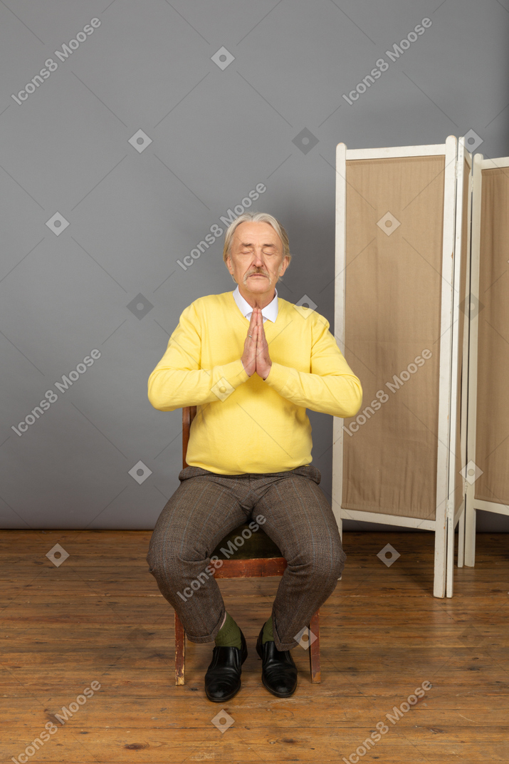 Mann sitzt mit gefalteten händen und geschlossenen augen