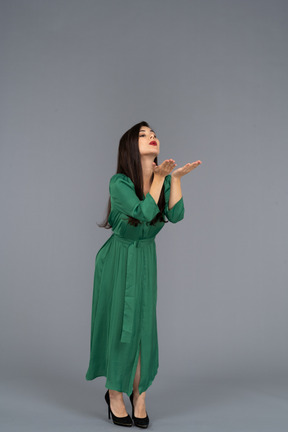 Vista di tre quarti di una giovane donna in abito verde che invia un bacio d'aria