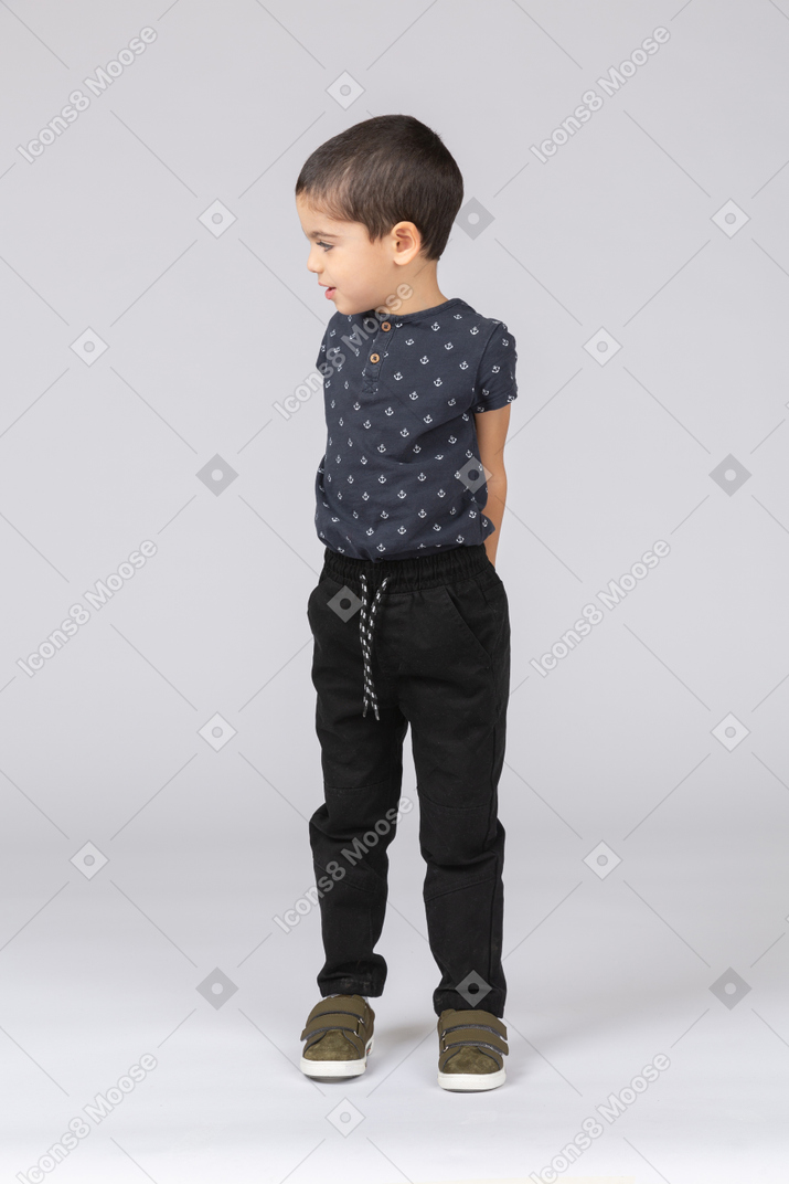 Front view of a cute boy posing with hands behind back and looking aside