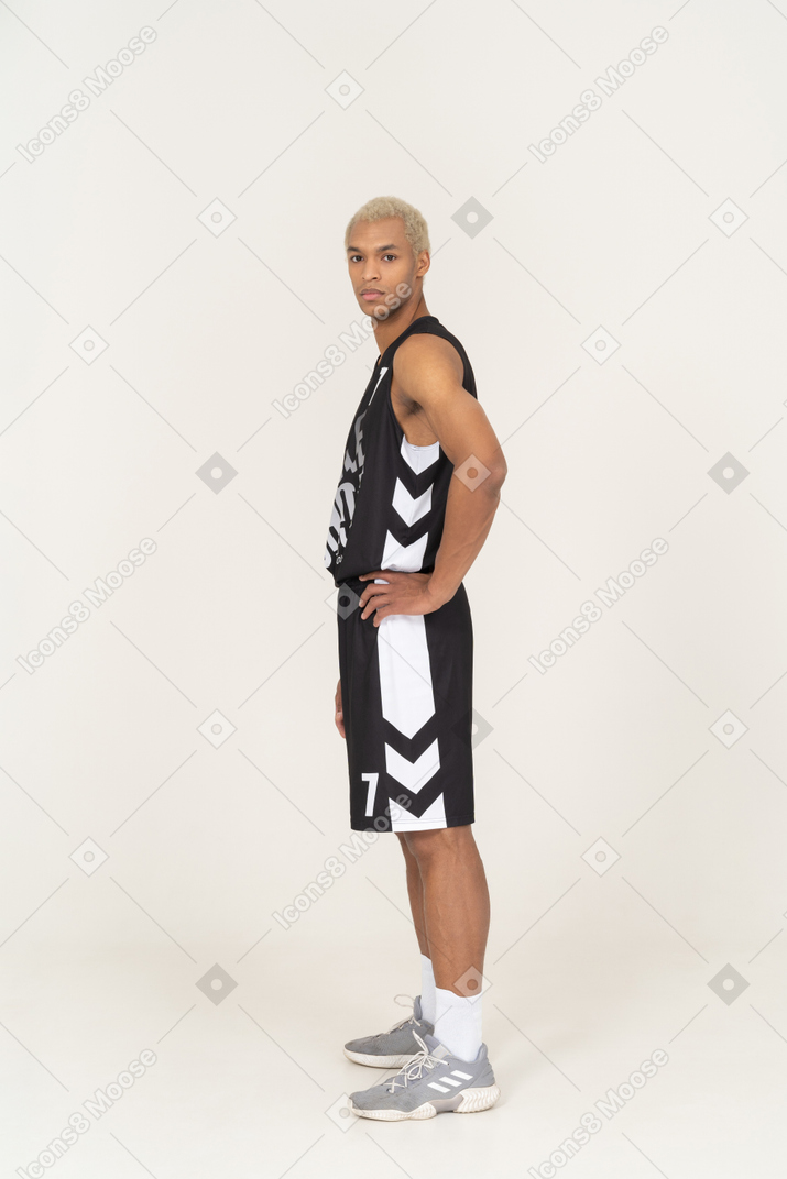 Vista lateral de un joven jugador de baloncesto masculino poniendo las manos en las caderas
