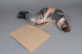 Young man lying down wrapped in plastic