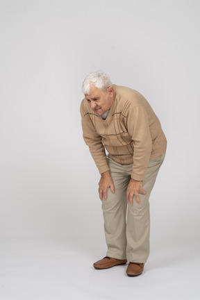 Front view of an old man bending down and touching his hurting knees