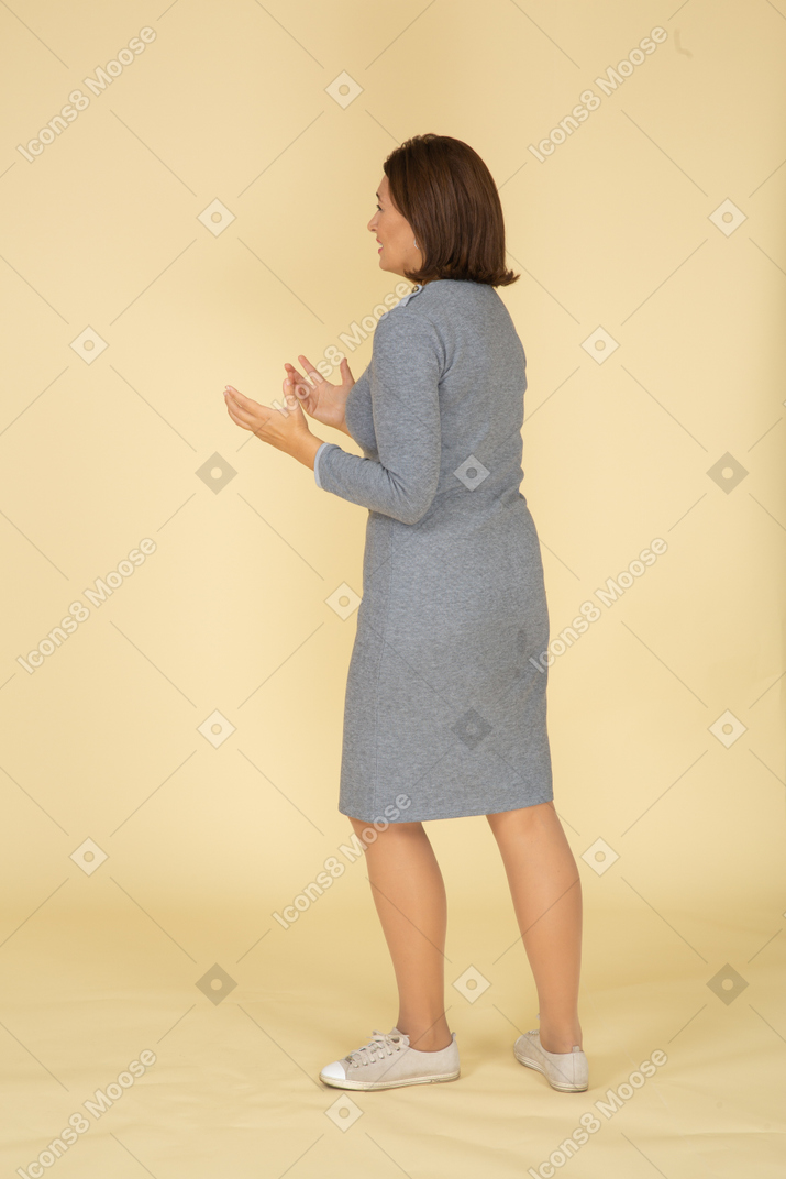 Женщина в сером платье жестикулирует, вид сбоку